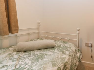 A bed with a white metal frame a rolled towel and a patterned bedspread near a window with beige curtains at Machlud Haul in Llwyngwril