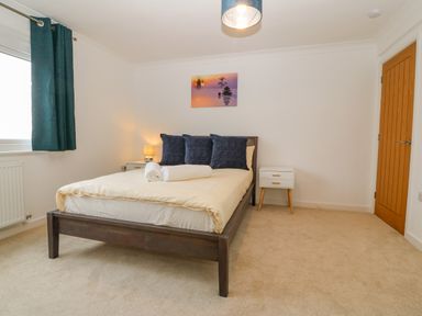 A bedroom with a bed three dark pillows two rolled towels bedside tables a lamp and a wooden door at Machlud Haul in Llwyngwril