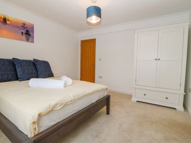 A bedroom with a bed with rolled towels on it a white wardrobe a wooden door and a painting on the wall at Machlud Haul in Llwyngwril