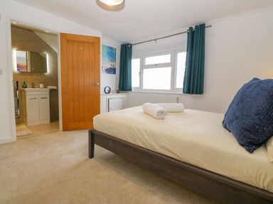 A bedroom with a bed, two rolled towels, a window with curtains, a wooden door, and an adjoining bathroom at Machlud Haul in Llwyngwril