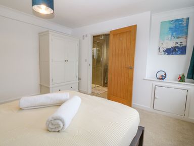 A bedroom with a white wardrobe a bed with rolled white towels an open wooden door leading to a bathroom and a small decorated window ledge at Machlud Haul in Llwyngwril