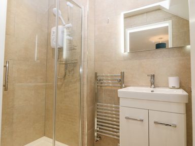 A bathroom with a glass shower enclosure a white sink with a cabinet a towel radiator and a mirror with light at Machlud Haul in Llwyngwril