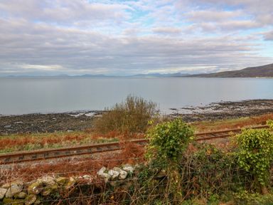 A coastal scene with railway tracks and vegetation near the shore at Machlud Haul in Llwyngwril
