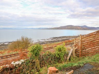 A view of a coastal landscape with railway tracks a wooden fence and hills in the distance at Machlud Haul in Llwyngwril