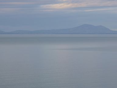 A large body of calm water with hills in the distance under a cloudy sky at Machlud Haul in Llwyngwril