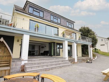 The exterior of a two-story house with a balcony and outdoor seating area with steps leading to an open living space at Machlud Haul in Llwyngwril