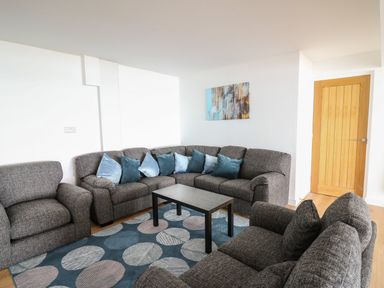 A living room with gray sofas blue cushions a black coffee table and a circular pattern rug at Machlud Haul in Llwyngwril