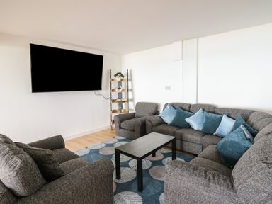 A living room with grey sofas blue cushions a black coffee table and a wall-mounted TV at Machlud Haul in Llwyngwril