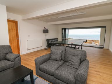 A room with gray sofas a table tennis table a black sofa and a large window showing a sea view at Machlud Haul in Llwyngwril