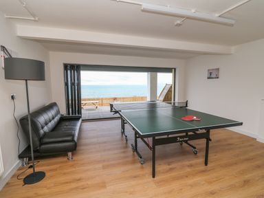 A game room with a ping pong table two paddles a black sofa and floor lamp with sea view at Machlud Haul in Llwyngwril