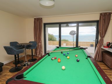 A room with a pool table and chairs near sliding glass doors overlooking the sea at Machlud Haul in Llwyngwril