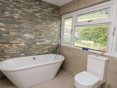 A bathroom with a bathtub a toilet a window and a stone tiled wall at Machlud Haul in Llwyngwril