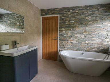 A bathroom with a freestanding bathtub a wall-mounted sink with a cabinet a large mirror and a wooden door at Machlud Haul in Llwyngwril
