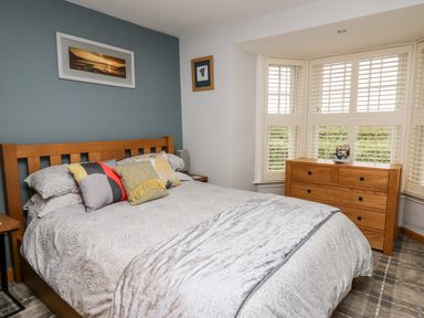 A bedroom with a wooden bed with pillows and a blanket a wooden dresser and windows with shutters at Dolwern in Dinas Cross