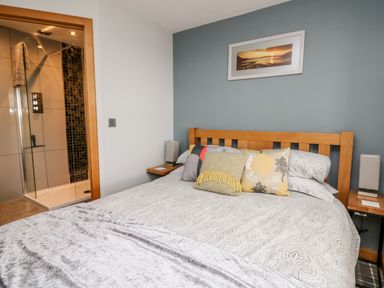 A bedroom with a wooden bed frame patterned bedding multiple pillows two bedside shelves with lamps and a shower room visible through an open door at Dolwern in Dinas Cross