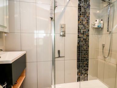 A bathroom with a sink and a shower area with glass partition and wall tiles at Dolwern in Dinas Cross
