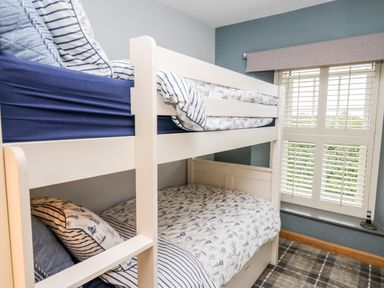A bedroom with a white bunk bed and window with shutters at Dolwern in Dinas Cross