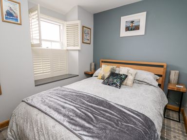 A bedroom with a bed with multiple pillows beside a window with shutters at Dolwern in Dinas Cross