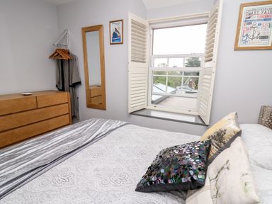 A bedroom with a bed near a window with shutters a wooden dresser a wall mirror and hanging clothes at Dolwern in Dinas Cross