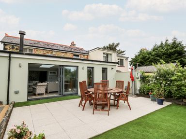A patio with wooden table and chairs outside modern house with garden and plants at Dolwern in Dinas Cross