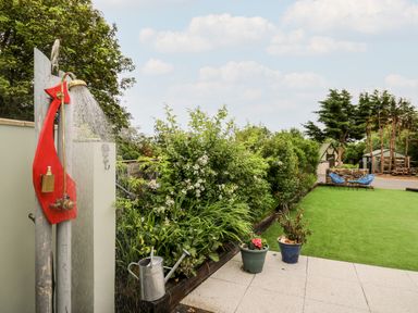 An outdoor garden area with a shower, watering can, potted plants, shrubs, green lawn, and blue chairs at Dolwern in Dinas Cross