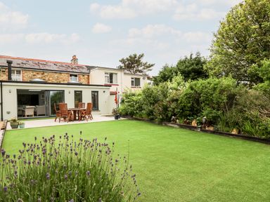 A backyard with green lawn patio table and chairs and shrubs at Dolwern in Dinas Cross