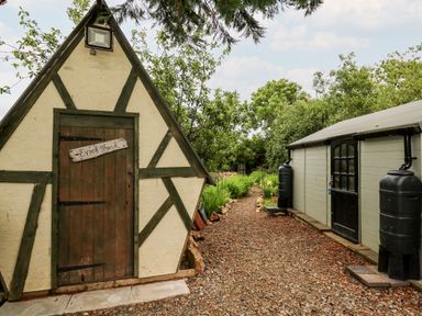 A triangular wooden shed named Evies Shack next to a rectangular wooden building with rainwater barrels at Dolwern in Dinas Cross