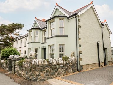 A stone-walled house with multiple windows and a paved driveway at Dolwern in Dinas Cross