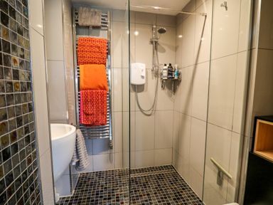 A bathroom with a shower area with glass divider towels on a heated rack and a small sink at Dolwern in Dinas Cross
