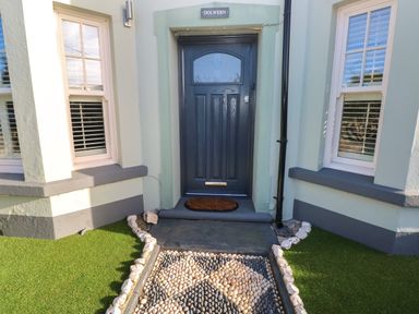 A front door with a doormat between two windows and pebble pathway at Dolwern in Dinas Cross