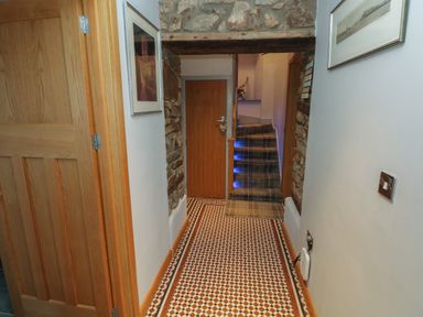 A hallway with tiled floor wooden doors stone wall accents and stairs with carpet at Dolwern in Dinas Cross