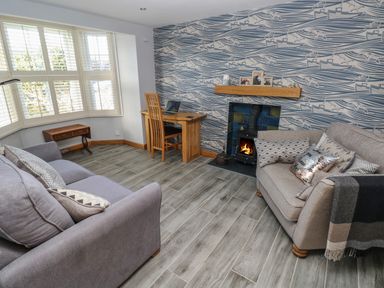 A living room with two sofas a wood burning stove and a wooden desk at Dolwern in Dinas Cross