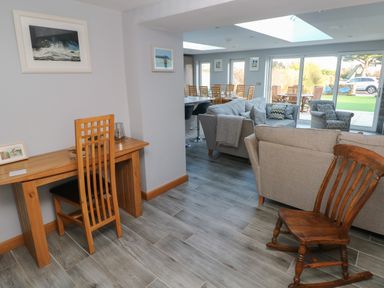 A living area with wooden desk and chair a rocking chair sofas and dining table near large windows at Dolwern in Dinas Cross