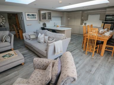 An open plan living room kitchen and dining area with sofas and a wooden dining table set with dishes at Dolwern in Dinas Cross