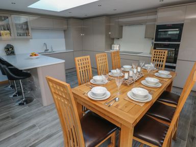 A dining table set with plates glasses and cutlery in a kitchen with cabinets and bar stools at Dolwern in Dinas Cross