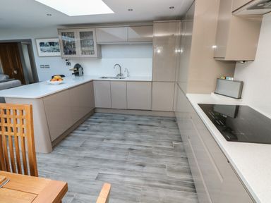 A kitchen with gray cabinets white countertops an electric stove a sink and wooden chairs at Dolwern in Dinas Cross