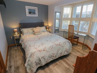 A bedroom with a bed two bedside tables lamps a glass desk wooden chair and a window with shutters at Dolwern in Dinas Cross