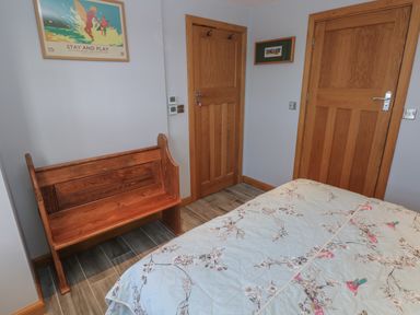 A bedroom with a floral bedspread a wooden bench two wooden doors and framed artwork on the walls at Dolwern in Dinas Cross