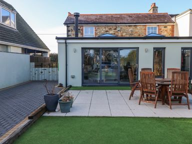 A backyard with patio tiles wooden outdoor table and chairs potted plants and sliding glass doors at Dolwern in Dinas Cross