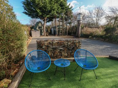 Two blue chairs and a blue table on artificial grass with a stone and metal divider and garden sheds in the background at Dolwern in Dinas Cross
