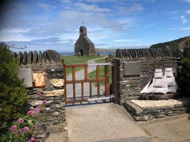 A stone gate with wooden gate leading to a stone building with a bell tower near the coast
