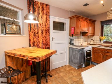 A kitchen with wooden cabinets a stove a sink and a small wooden table with a metal chair at Llys-Yr-Onnen in Carmarthen