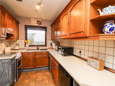 A kitchen with wooden cabinets tiled walls a window microwave toaster radio and kettle at Llys-Yr-Onnen in Carmarthen