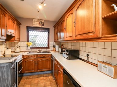 A kitchen with wooden cabinets a tiled backsplash a window with a vase of sunflowers and countertop appliances at Llys-Yr-Onnen in Carmarthen