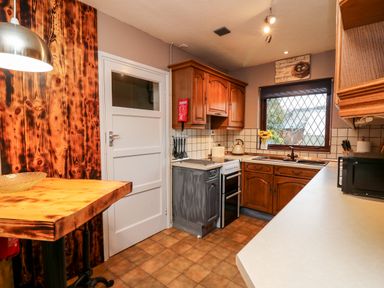 A kitchen with wooden cabinets a stove microwave and a window with a view at Llys-Yr-Onnen in Carmarthen