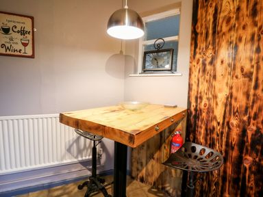 A small dining area with a wooden table metal stools a wall clock a fire extinguisher and a sign on the wall at Llys-Yr-Onnen in Carmarthen