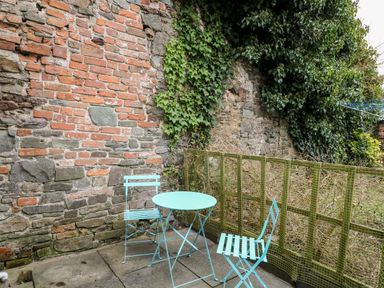 An outdoor patio area with a blue metal table and two chairs against a brick and stone wall with green ivy at Llys-Yr-Onnen in Carmarthen