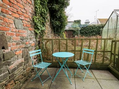 A small outdoor patio with two blue metal chairs and a round blue table near a brick wall and a garden at Llys-Yr-Onnen in Carmarthen
