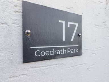 A black rectangular house number sign with 17 and Coedrath Park on a white textured wall at 17 Coedrath Park in Saundersfoot