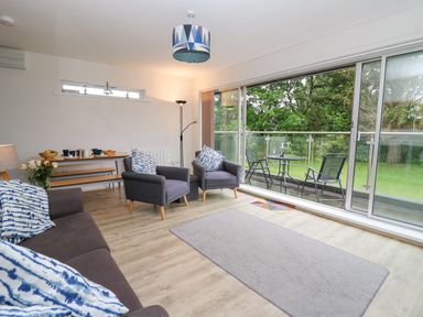A living room with grey chairs and a sofa with patterned cushions a small dining table a floor lamp and a balcony with outdoor chairs and table at 17 Coedrath Park in Saundersfoot
